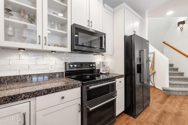 kitchen with appliances with stainless steel finishes, white cabinets, light hardwood / wood-style floors, backsplash, and dark stone counters