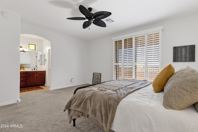 bedroom with ensuite bath, light colored carpet, ceiling fan, and sink