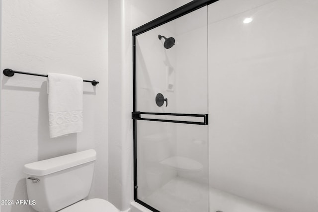 bathroom featuring a shower with shower door and toilet