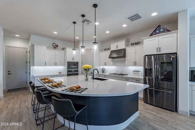 kitchen featuring appliances with stainless steel finishes, sink, light hardwood / wood-style floors, white cabinetry, and hanging light fixtures