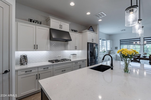 kitchen with light stone counters, black refrigerator with ice dispenser, sink, decorative light fixtures, and stainless steel gas stovetop