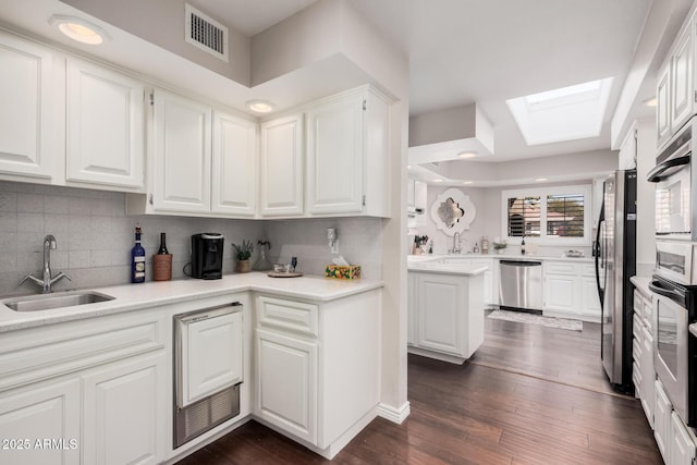 kitchen with sink, dark wood-type flooring, a skylight, stainless steel appliances, and white cabinets