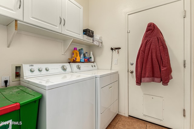 clothes washing area with cabinets, light tile patterned floors, and washing machine and clothes dryer