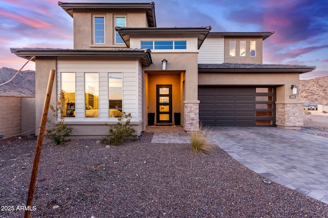 prairie-style house featuring stone siding, decorative driveway, and stucco siding