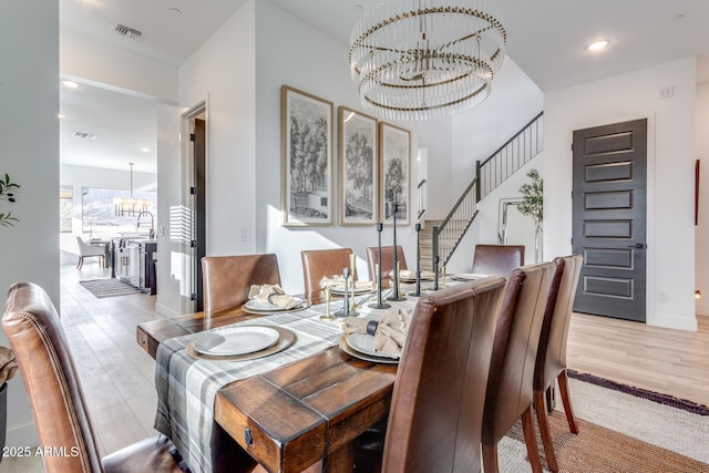 dining area featuring stairs, light wood-type flooring, visible vents, and an inviting chandelier