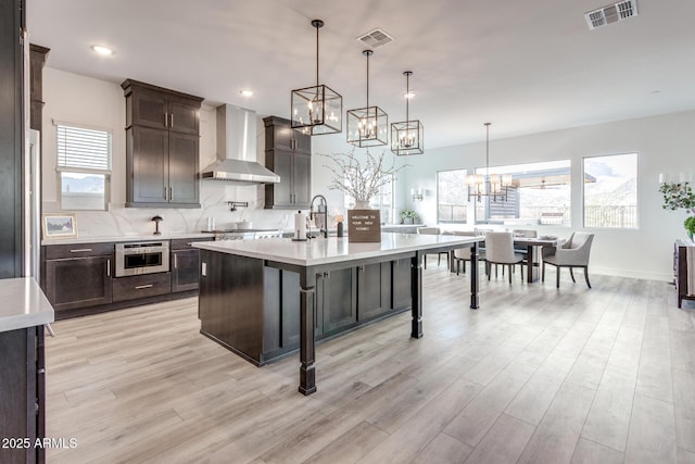 kitchen with a center island with sink, a breakfast bar area, light countertops, visible vents, and wall chimney exhaust hood