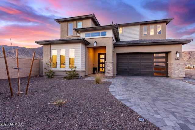 view of front of house featuring decorative driveway, an attached garage, a mountain view, fence, and stone siding