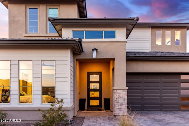 doorway to property with stone siding, decorative driveway, and stucco siding