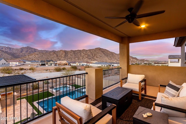 balcony at dusk featuring a pool with connected hot tub, a residential view, a mountain view, and an outdoor living space with a fire pit