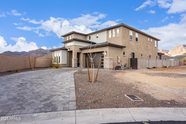 view of front of home with decorative driveway, stucco siding, an attached garage, a mountain view, and fence