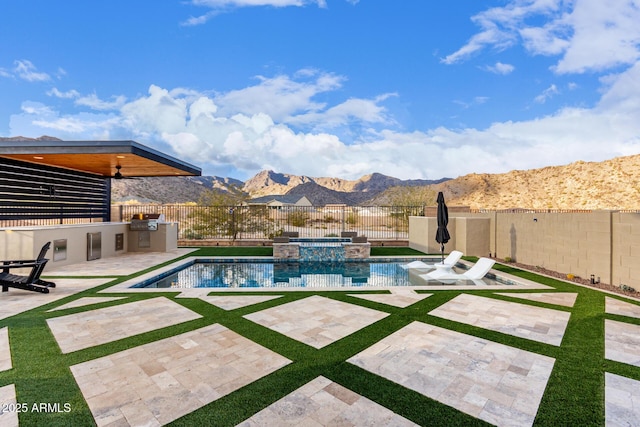 view of pool featuring a fenced backyard, a mountain view, a pool with connected hot tub, exterior kitchen, and a patio area