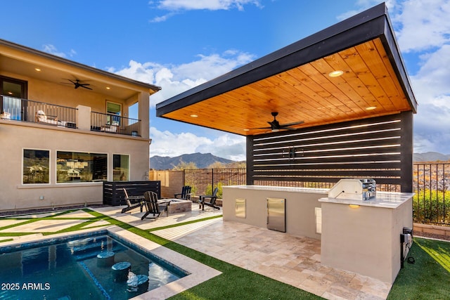 view of patio / terrace featuring a fire pit, a balcony, ceiling fan, exterior kitchen, and a mountain view