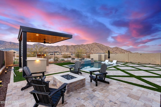 view of patio / terrace featuring ceiling fan, an outdoor fire pit, a fenced backyard, and a mountain view