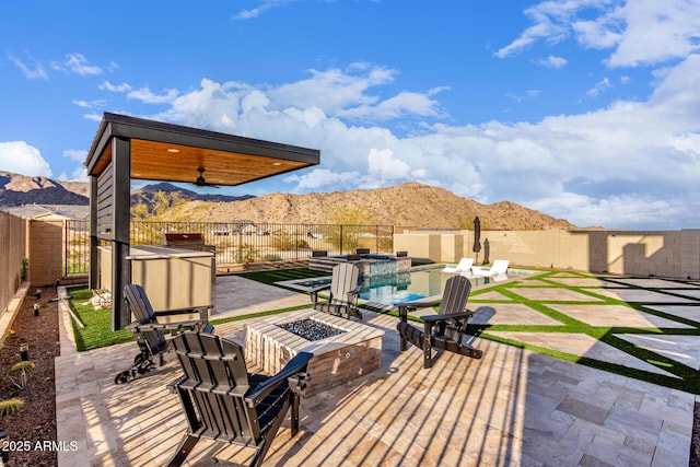 view of patio / terrace featuring ceiling fan, an outdoor fire pit, a fenced backyard, a mountain view, and a fenced in pool