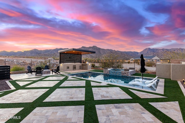 view of swimming pool featuring a pool with connected hot tub, a patio area, fence, and a mountain view