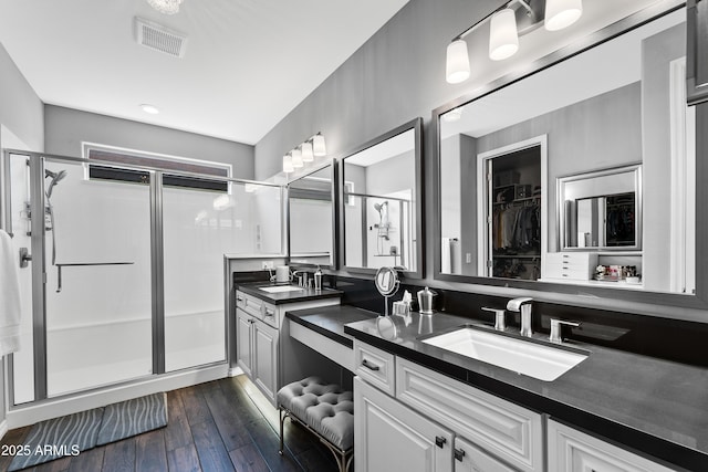 bathroom with wood-type flooring, visible vents, a sink, and a stall shower