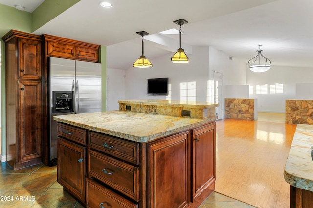 kitchen with hardwood / wood-style floors, stainless steel fridge, light stone counters, and pendant lighting