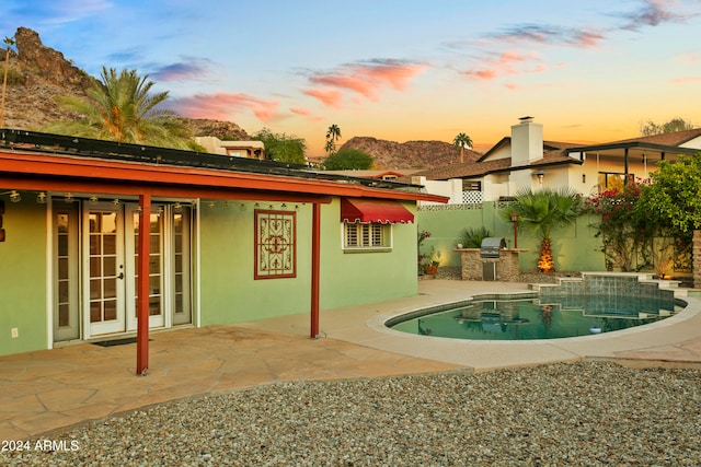 pool at dusk featuring exterior kitchen and a patio