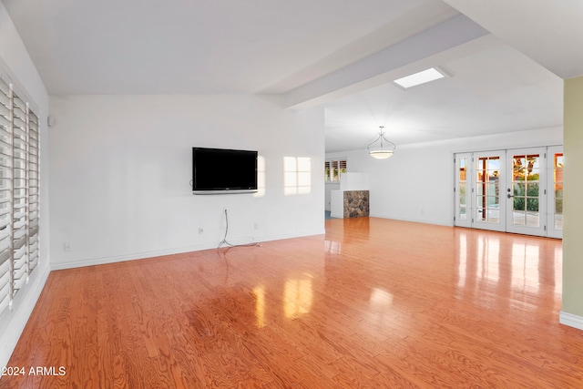 unfurnished living room with vaulted ceiling, light wood-type flooring, and french doors