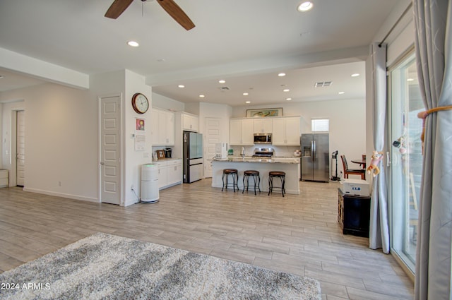 kitchen featuring a kitchen island with sink, a breakfast bar, white cabinets, and appliances with stainless steel finishes