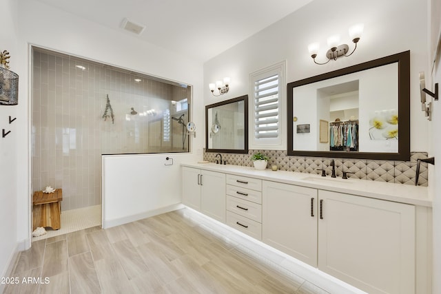 bathroom with a tile shower, vanity, and backsplash