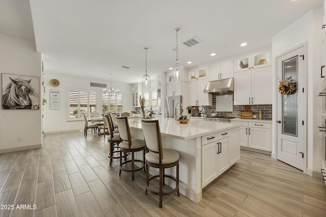 kitchen featuring a kitchen island with sink, white cabinets, pendant lighting, and an inviting chandelier