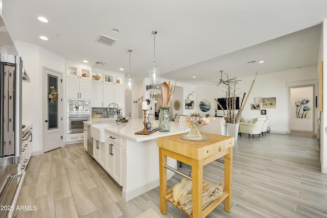 kitchen featuring backsplash, a kitchen island with sink, sink, pendant lighting, and white cabinetry