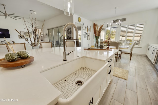 kitchen with pendant lighting, ceiling fan with notable chandelier, sink, a kitchen island, and white cabinetry