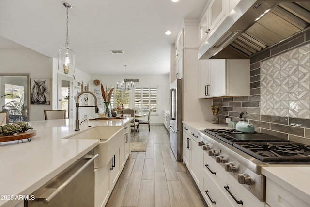 kitchen featuring white cabinetry, sink, ventilation hood, decorative light fixtures, and appliances with stainless steel finishes