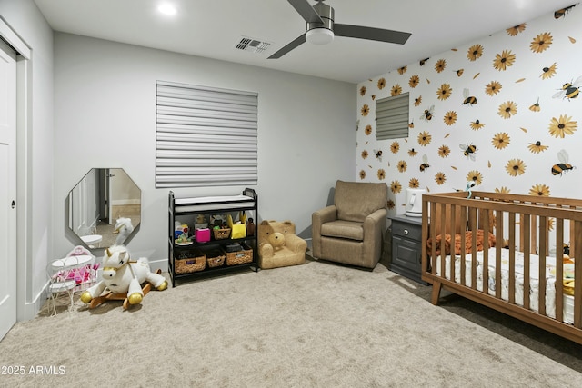 carpeted bedroom featuring visible vents, a ceiling fan, a crib, baseboards, and wallpapered walls