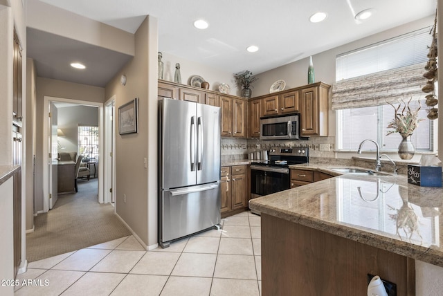 kitchen with light stone counters, kitchen peninsula, stainless steel appliances, light carpet, and sink