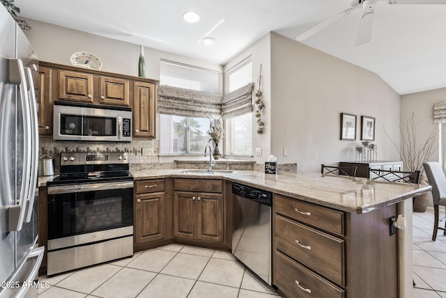 kitchen featuring sink, stainless steel appliances, light stone counters, and kitchen peninsula