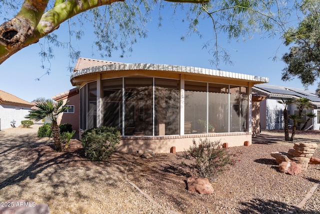 back of property with a sunroom and solar panels