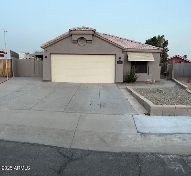 view of front of house with a garage, concrete driveway, a tiled roof, fence, and stucco siding