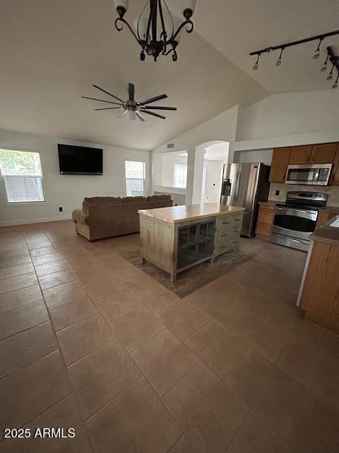 unfurnished living room featuring a wealth of natural light, arched walkways, track lighting, and ceiling fan with notable chandelier