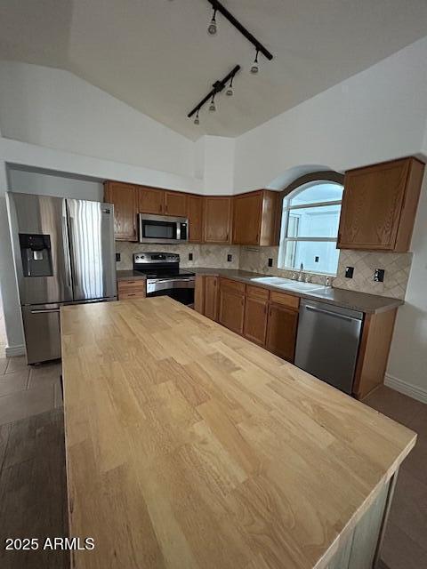 kitchen with butcher block counters, decorative backsplash, appliances with stainless steel finishes, brown cabinetry, and a sink