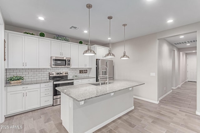 19873 W San Juan Ave, Litchfield Park, AZ 85340 - kitchen featuring stainless steel appliances, a sink, white cabinetry, decorative backsplash, and an island with sink