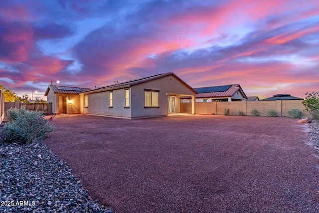 19873 W San Juan Ave, Litchfield Park, AZ 85340 - back of property at dusk with a fenced backyard, roof mounted solar panels, stucco siding, and a patio area