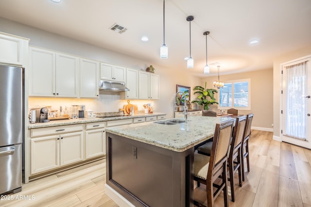 kitchen with visible vents, freestanding refrigerator, light wood-type flooring, under cabinet range hood, and a sink