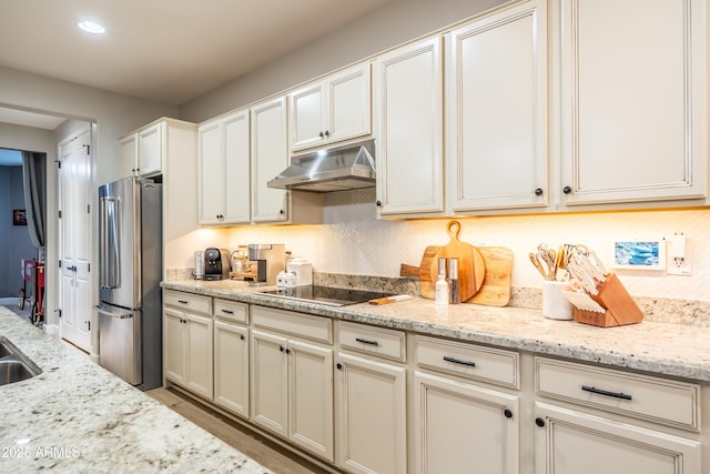 kitchen featuring under cabinet range hood, black electric stovetop, backsplash, and freestanding refrigerator