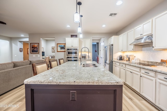 kitchen featuring tasteful backsplash, visible vents, appliances with stainless steel finishes, under cabinet range hood, and a sink