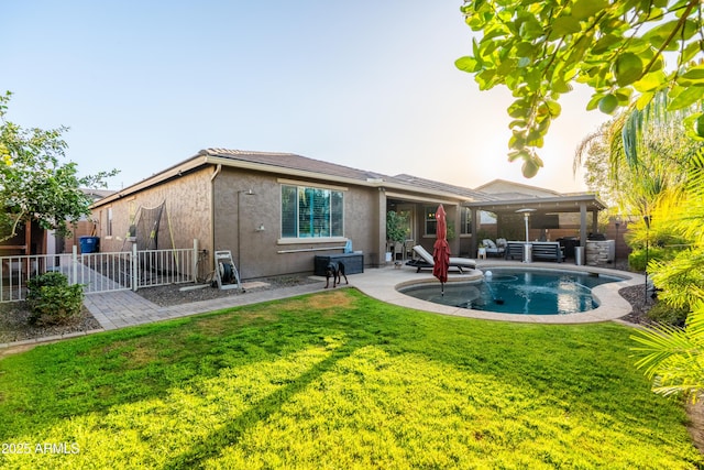 rear view of property featuring a patio, fence, a lawn, and stucco siding