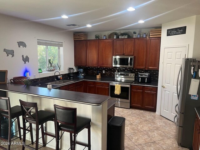 kitchen featuring backsplash, kitchen peninsula, sink, a breakfast bar, and appliances with stainless steel finishes