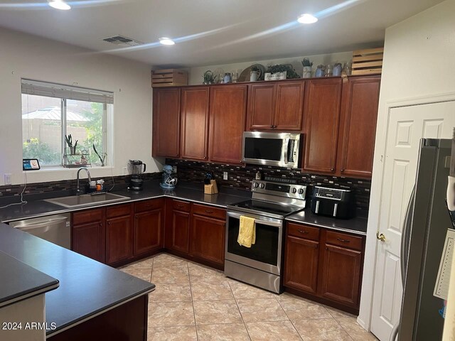 kitchen with appliances with stainless steel finishes, tasteful backsplash, sink, and light tile patterned flooring