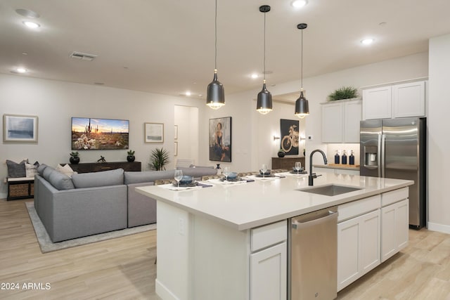 kitchen featuring stainless steel appliances, white cabinets, a sink, light wood-type flooring, and open floor plan