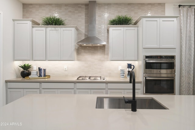 kitchen featuring decorative backsplash, stainless steel appliances, light countertops, a sink, and wall chimney exhaust hood