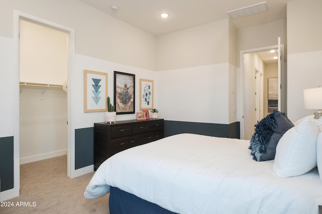 bedroom featuring visible vents, a closet, baseboards, light carpet, and a walk in closet