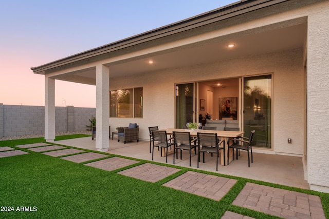 back of house at dusk featuring a lawn, fence, stucco siding, and a patio area