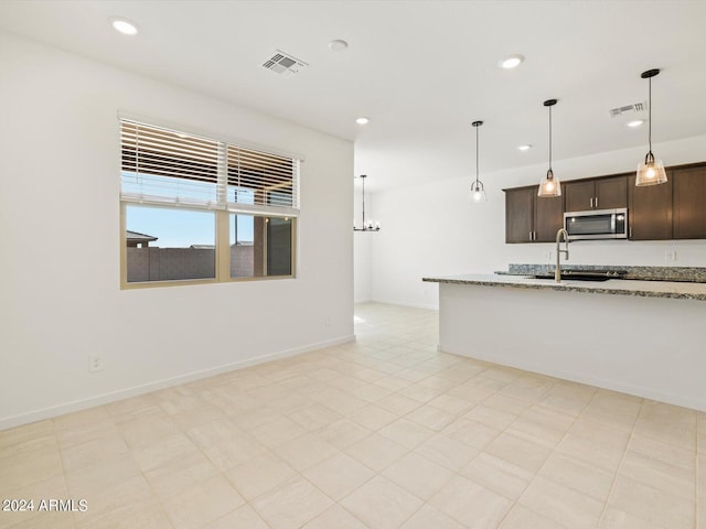 kitchen featuring decorative light fixtures, dark brown cabinetry, light stone counters, and sink