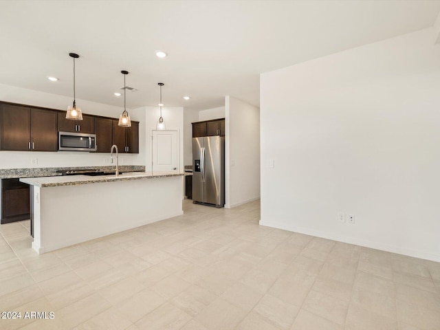 kitchen featuring light stone countertops, appliances with stainless steel finishes, an island with sink, dark brown cabinets, and decorative light fixtures